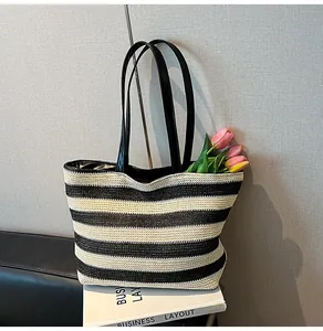 Detail of large striped woven tote bag with straw texture and black faux leather handles