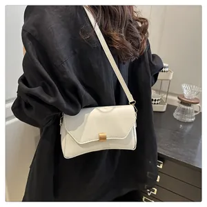 Détail du sac bandoulière en cuir blanc avec boucle dorée porté à l'épaule de la femme
