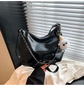 Detail of glossy black leather tote bag with silver chain and white plush charm