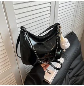 Detail of glossy black faux leather hobo bag with metal chain strap and cute white charm