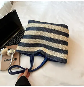 Detail view of a striped woven tote bag featuring navy blue leather handles and large capacity