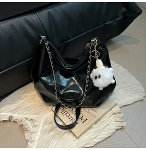 Glossy black tote bag detail with silver chain strap and plush monster charm