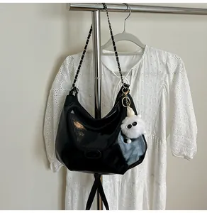 Detail of glossy black tote bag with chain strap and plush monster charm on lace background