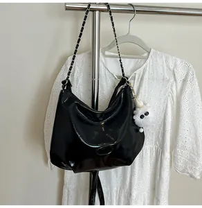 Detail of glossy black tote bag with metal chain strap and cute white plush charm