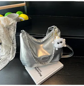 Detail of silver metallic hobo bag featuring chain strap and plush monster charm