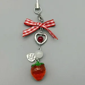 Close-up of strawberry phone charm with bow and engraved Made with Love heart tag