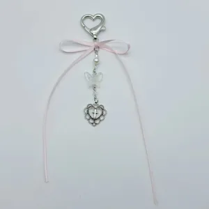 Detail von rosa Schleife und silbernem Herzanhänger mit Kreuz an einer Perlen-Handykette