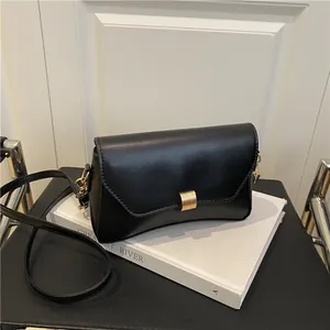 Sac à bandoulière en cuir noir minimaliste avec boucle dorée sur des livres blancs