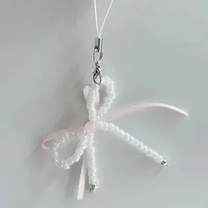 Detail of balletcore beaded phone charm with white beads, pink ribbon and silver clasp