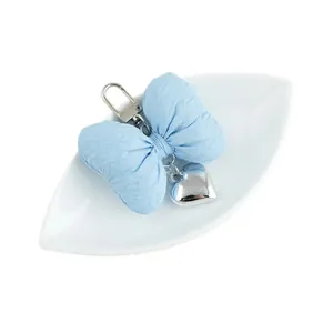 Blue bow keychain with silver heart pendant on a white leaf-shaped ceramic tray