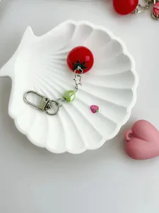 Detail of red tomato charm with green heart bead and silver metal clasp on white tray