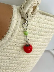 Detail of red tomato charm with a silver star and green heart on a woven straw bag