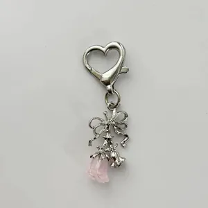 Detail of silver bow and heart clasp keychain with pink rose petal charms on white base