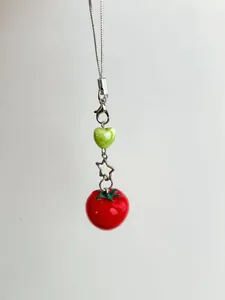 Detail of red tomato pendant with star metal ring and green heart bead on phone strap