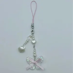 Pink ribbon bow phone charm with pearls, shell pendant, and iridescent butterfly detail