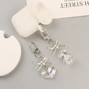 Iridescent bear and heart keychain charms with silver clasp on a white earphone case