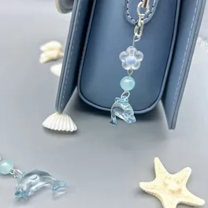 Taschenanhänger Delphin aus blauem Harz mit Blumenperle an einer Lederhandtasche
