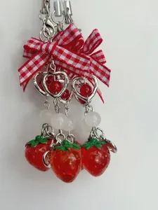 Detail of strawberry charm with red plaid bow and silver heart frame pendant