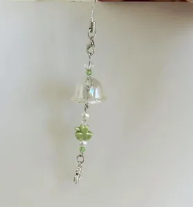 Detail of handmade clover phone charm with green beads, ceramic petals and silver bell