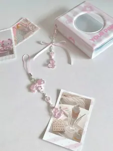 Chaîne de téléphone en perles roses avec nœud et pendentif ours à côté d'un album photo
