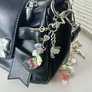 Détail d'un charm de téléphone perlé avec pêche rose et fermoir étoile sur un sac noir