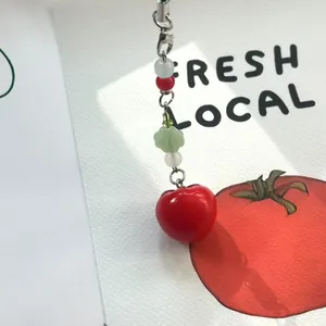 Detailed view of handmade tomato beaded keychain with red resin fruit and green cloud bead