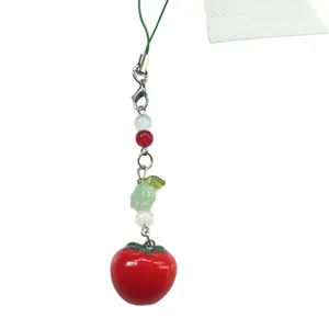 Glossy red tomato pendant with tri-color beads and green leaf on white background