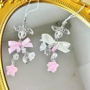 Handmade phone charms with pink bows, angel wings, stars, and beads on a mirror surface