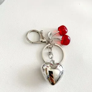 Portachiavi creativo con ciliegie rosse e ciondolo a cuore argentato su pelle bianca