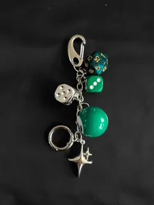 Detail of retro dice keychain with green 8-ball and silver star charms on black background