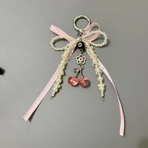 Pink ribbon bow keychain with pearls and cherry charms on a grey background