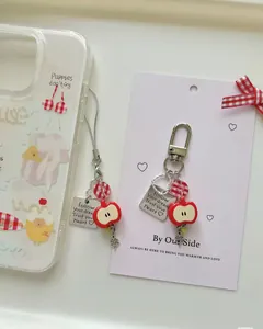 Detail of red apple keychain with heart tag and clover pendant on phone case