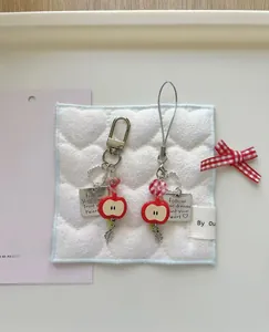 Detail of red apple charm with metal engraved tag and red ribbon on quilted background