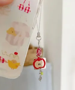 Macro view of handmade phone charm featuring a red apple pendant and silver clover detail