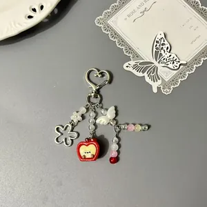 Cute apple heart keychain with metal flower, wings, and colorful bead charms on grey base