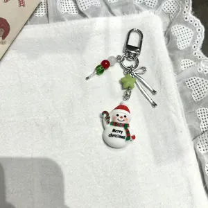 Porte-clés bonhomme de neige avec étoile verte et nœud rouge sur fond festif en dentelle