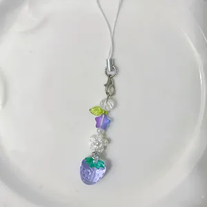 Cute purple strawberry beaded phone charm with flower and star beads on white ceramic tray