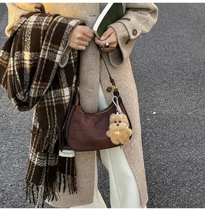 Outdoor shot of a brown suede half-moon bag with a plaid scarf and teddy charm