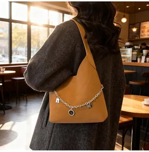 Brown leather tote bag featuring large silver metal chains and charms in a sunlit cafe