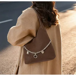Detail view of coffee suede tote bag with vintage metal charms on a model in a beige coat