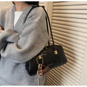 Detalle de bolso de hombro en cuero negro con herrajes dorados y mini colgante de bolso