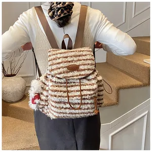 Detail eines gestreiften Plüschrucksacks mit Bärenanhänger und braunen Textilgurten