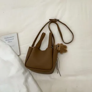 Brown bucket bag with pebble leather texture, crossbody strap and plush bear charm