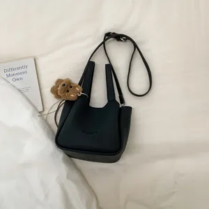Detail of black pebbled leather bucket bag with top handles and a brown plush bear charm