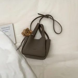 Overhead view of a taupe mini leather bucket bag with a cute brown plush bear charm