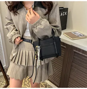 Detail of black crossbody bag with woven rope handle and metal chain decoration