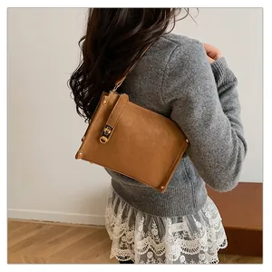 Détail du sac à bandoulière en daim marron avec fermoir doré sur pull gris chiné