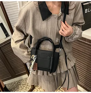 Detail of black faux leather handbag with braided handle and chocolate charm decoration