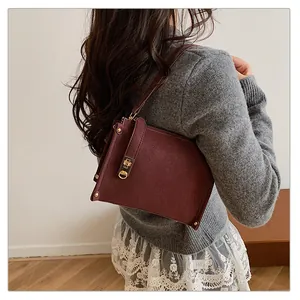 Détail du sac à bandoulière en cuir bordeaux avec boucle dorée et fermeture éclair
