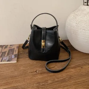 Vintage black leather bucket bag with gold lock on a rustic wooden table setting